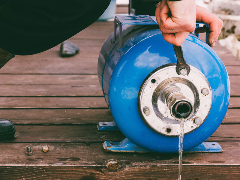Man holding a wrench next to a blue propane tank.